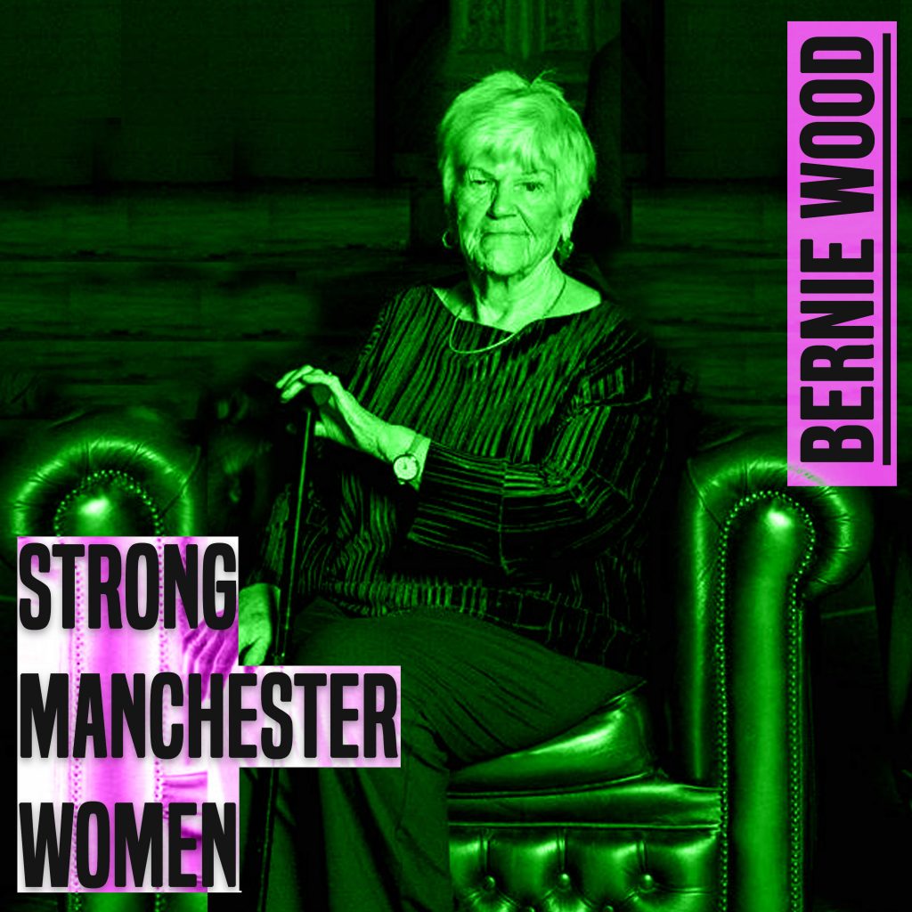 A photo of women sat in a leather Chesterfield style chair. The image is from her knees up. She is holding a walking stick. She is white. she is looking directly at the camera. She is wearing dark clothes. She has short white hair. The image has a green hue to it. to the left of her knees are the words 'strong manchester women' in grey lettering and a thick font in capital letters. In the same style font, next to her right ear are the words 'Bernie Wood'.