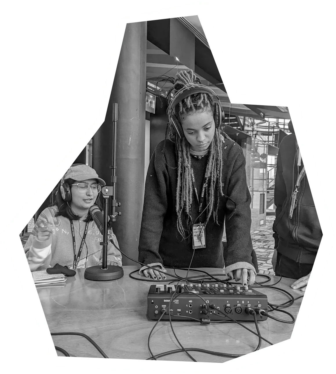 3 people around a table. 1 girl seated with headphones on. A male and young girl stand looking over a sound desk