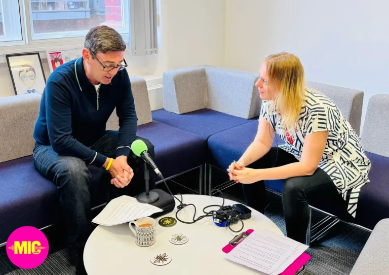 a man and a woman sit around a table, the man is speaking into a microphone