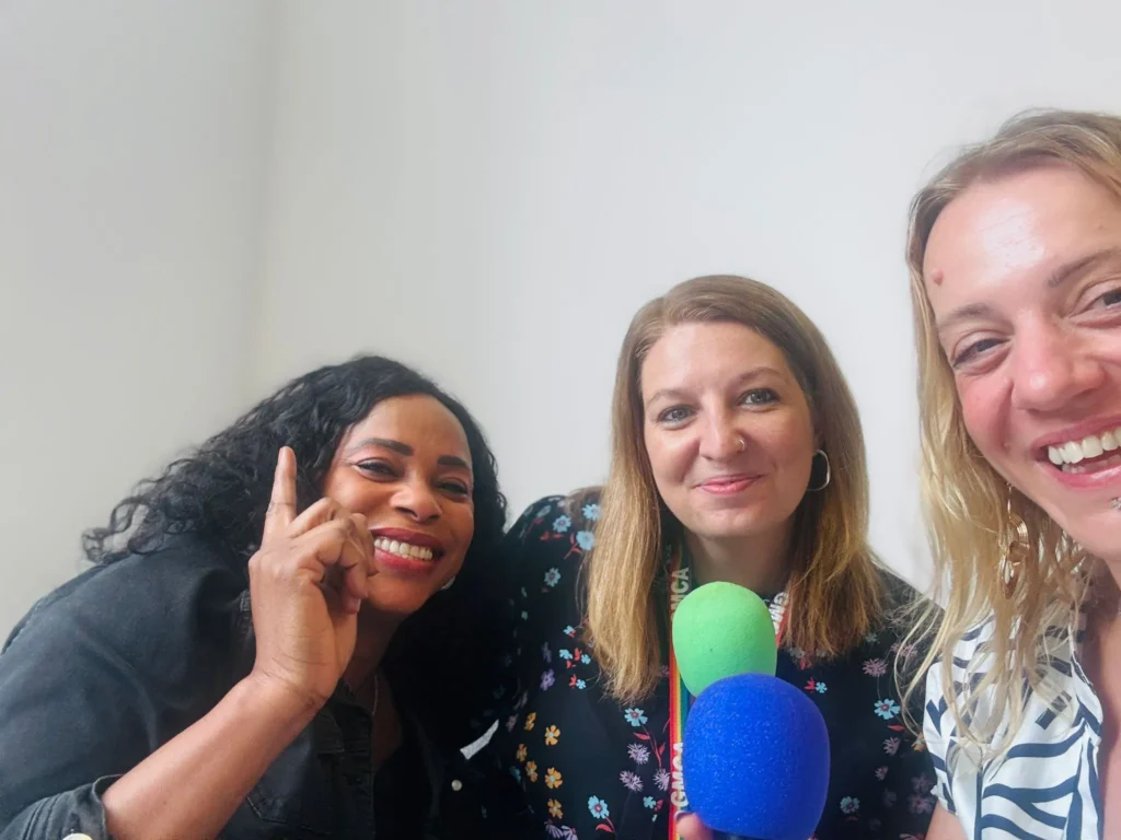 3 women smile at a camera and hold microphones