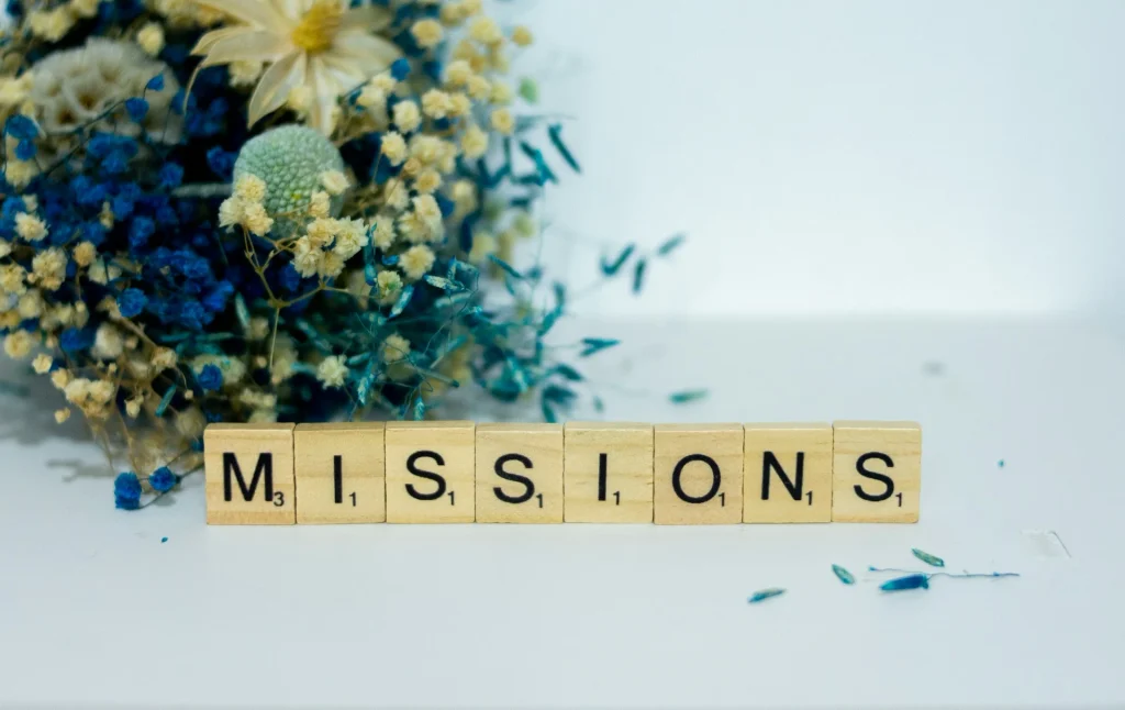 Wooden letter tiles spelling “missions” beside a bunch of flowers.