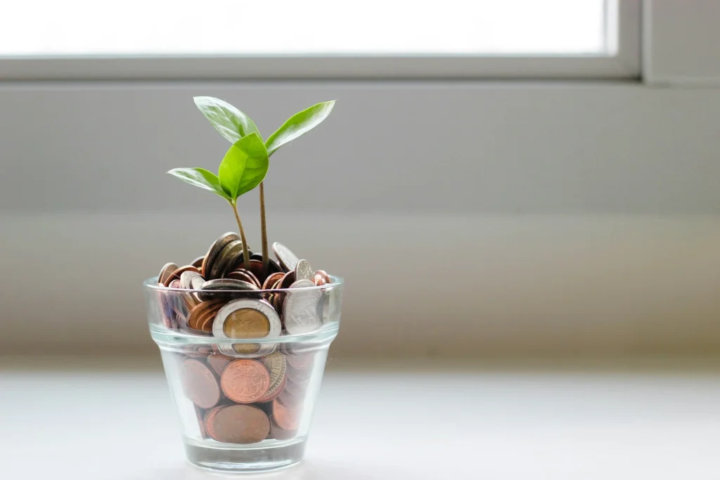 Small plant growing from a glass jar filled with coins.