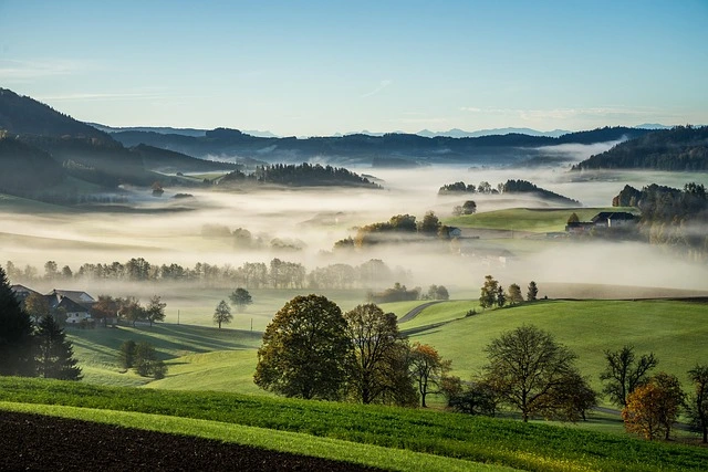 Wide landscape overlooking green hills, fields and distant mountains.