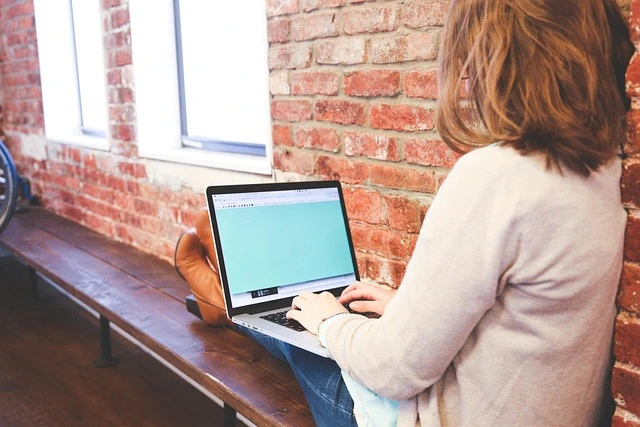 Woman working on a laptop at a desk beside a window.