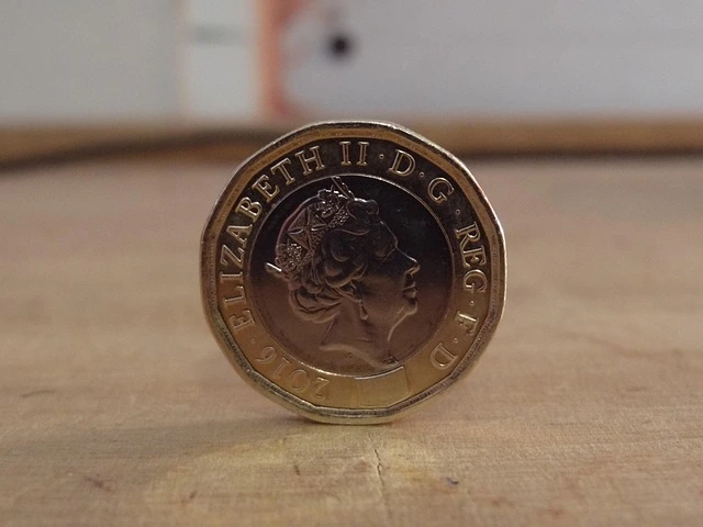 One pound coin standing upright on a wooden surface.